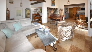 Sala de estar com sofá, mesa de centro e poltrona estampada. Há também um espaço de jantar com mesa e cadeiras.
