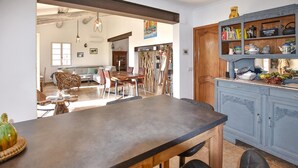 Uma cozinha com bancada de madeira, área de refeições com sofá e cadeiras, e um armário azul com utensílios de cozinha.
