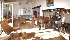 Uma sala de estar ampla com uma mesa de jantar, cadeiras, um sofá e uma poltrona de vime.