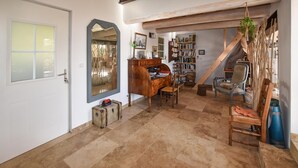 Um quarto aconchegante com uma escrivaninha de madeira, uma estante e uma cadeira. Há uma mala no chão e uma planta pendurada no teto.