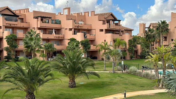 A multi-story hotel with a uniform architectural style, featuring balconies and a well-maintained lawn with palm trees.