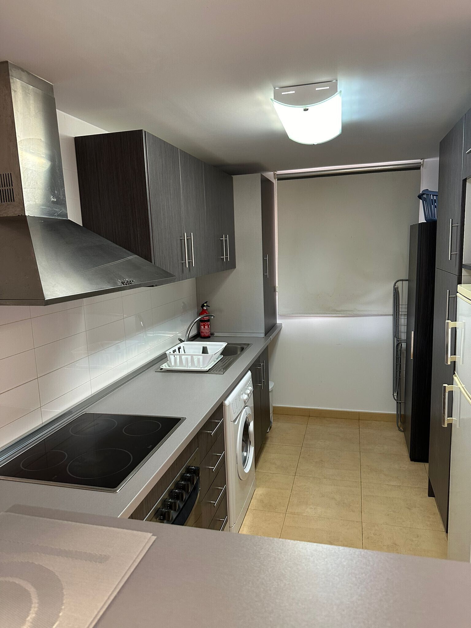 A modern kitchen with grey cabinets, a stainless steel stove, a built-in oven, and a washing machine.