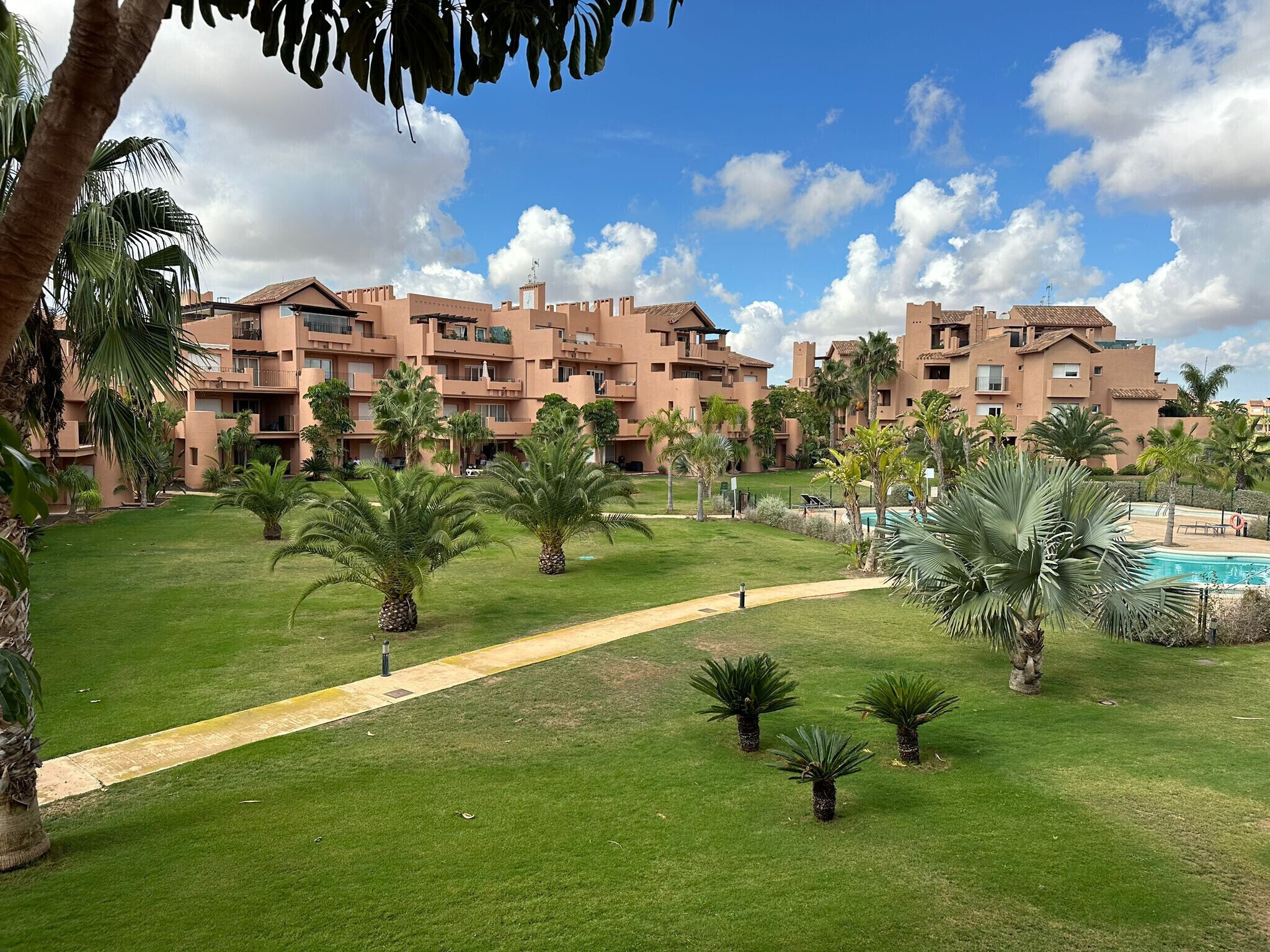A resort with multiple buildings, a swimming pool, and a well-maintained lawn with palm trees.