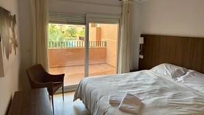 A hotel room with a bed, a chair, a ceiling fan, and a view of a pool and greenery outside.