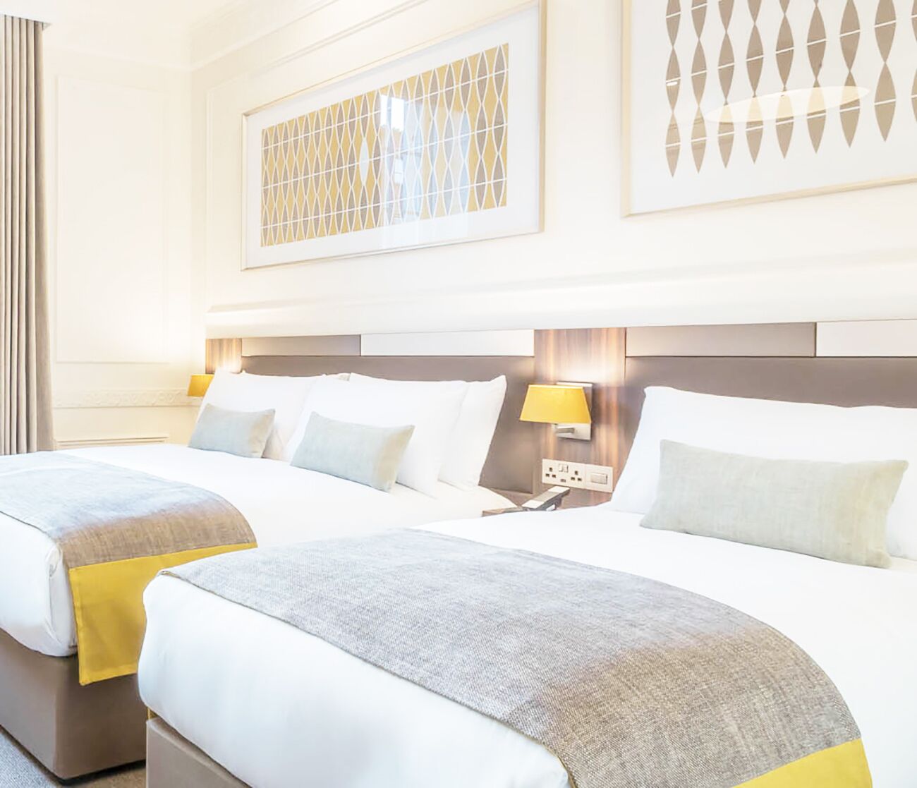 Habitación de hotel con dos camas, cabecera con lámpara y panel decorativo en la pared.