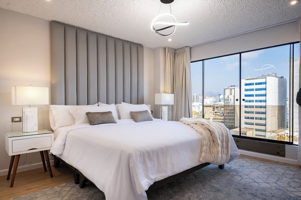 Une chambre d’hôtel moderne dotée d’un grand lit, offrant une vue sur la ville et présentant un design contemporain.