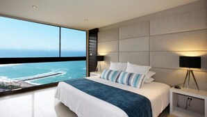 Un dormitorio moderno con una cama grande, vista al océano y al paisaje urbano.