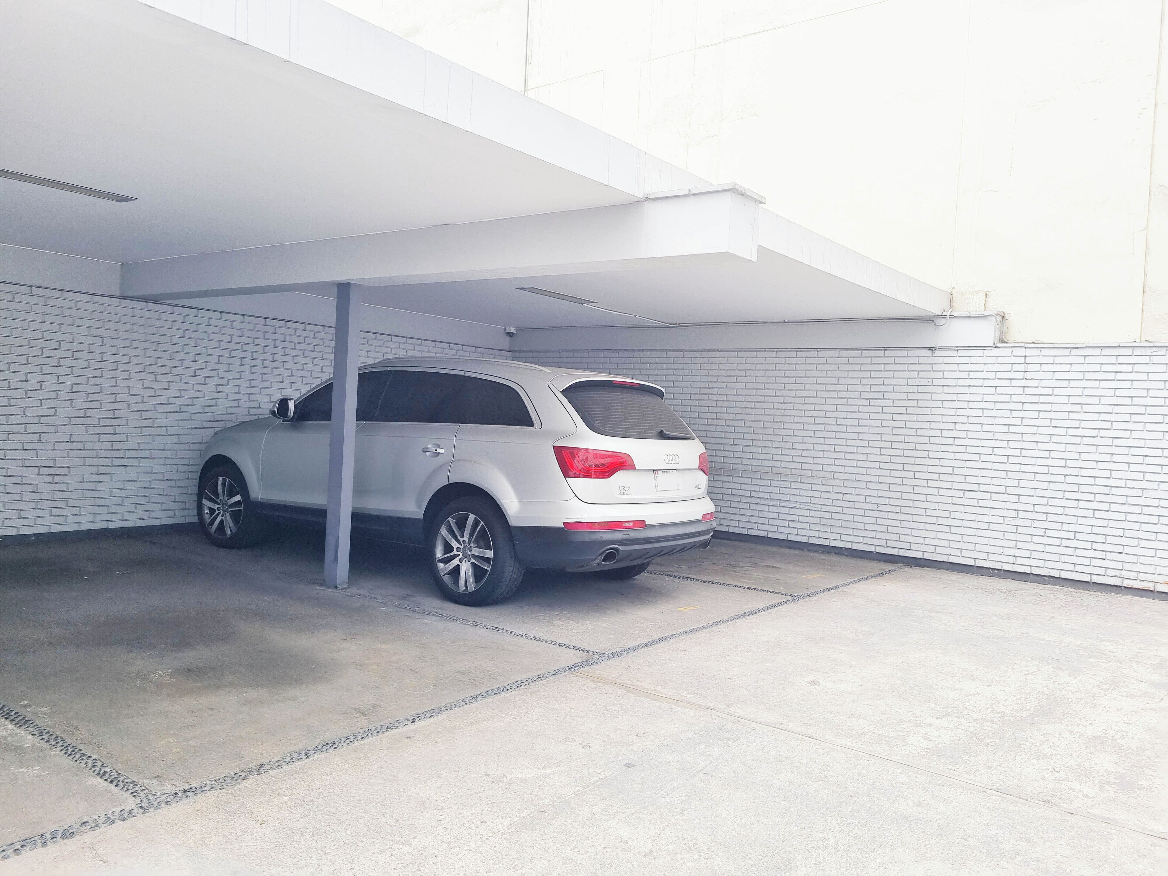 En vit SUV står parkerad på en överbyggd parkeringsplats med vita tegelväggar och ett betonggolv.
