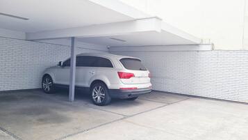 A white SUV parked in a covered parking area with white brick walls and a concrete floor.