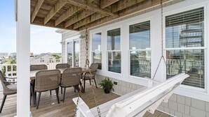 Ein überdachter Außenbereich mit Holzterrasse, Tisch und Stühlen sowie einer Hängeschaukel.