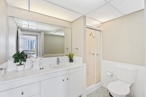 Une salle de bain moderne avec un grand miroir, des éléments d’ameublement blancs, une plante en pot et une vue sur la ville par la fenêtre.