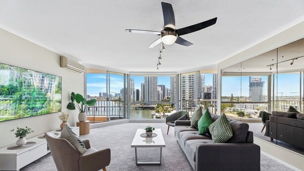 A spacious living room with a large window, a ceiling fan, and a view of the city skyline.