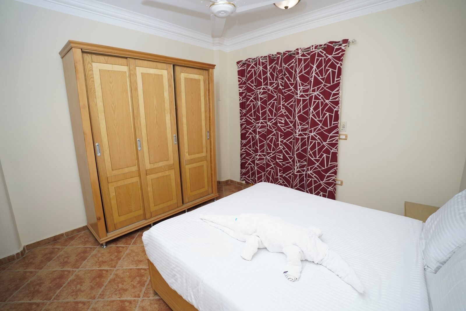 A bedroom with a bed, a wardrobe, and a red patterned curtain.