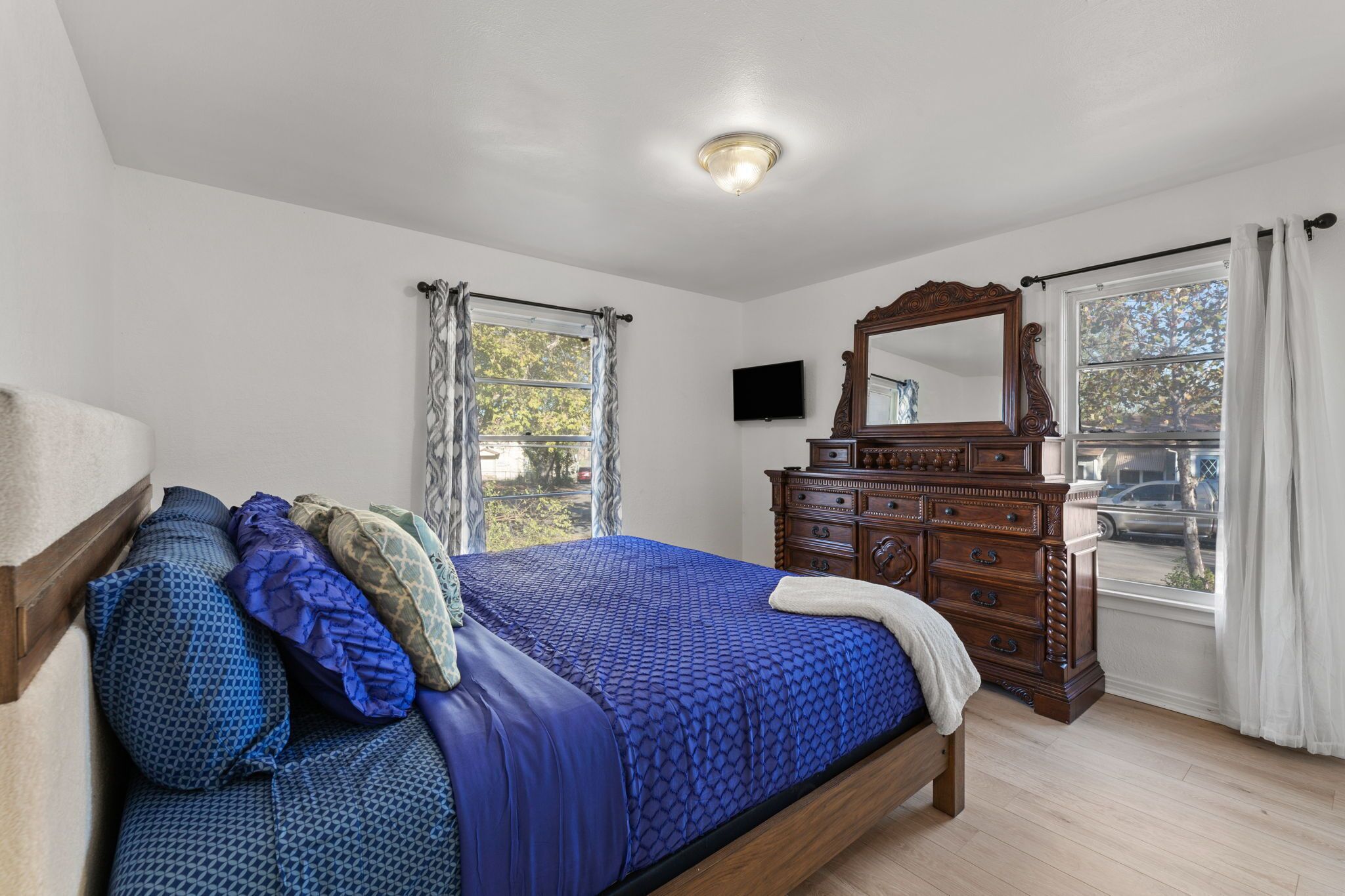 A bedroom with a large bed, wooden dresser, and a television on the wall.