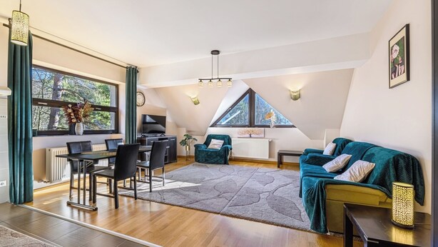 En rymlig loftlägenhet med ett matområde, ett vardagsrum med en grön soffa och ett stort fönster med utsikt över träd.