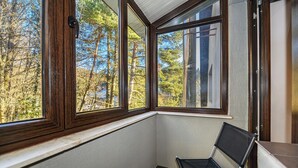 Ett hörnrum med utsikt över träd genom stora fönster, en stol och ett klinkergolv.