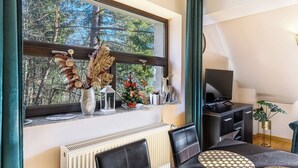 En matplats med ett bord, stolar, ett element, en tv och ett fönster med utsikt över träd.