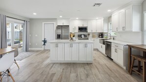 Una cocina moderna con armarios blancos, una isla central, electrodomésticos de acero inoxidable y una mesa de comedor de madera.