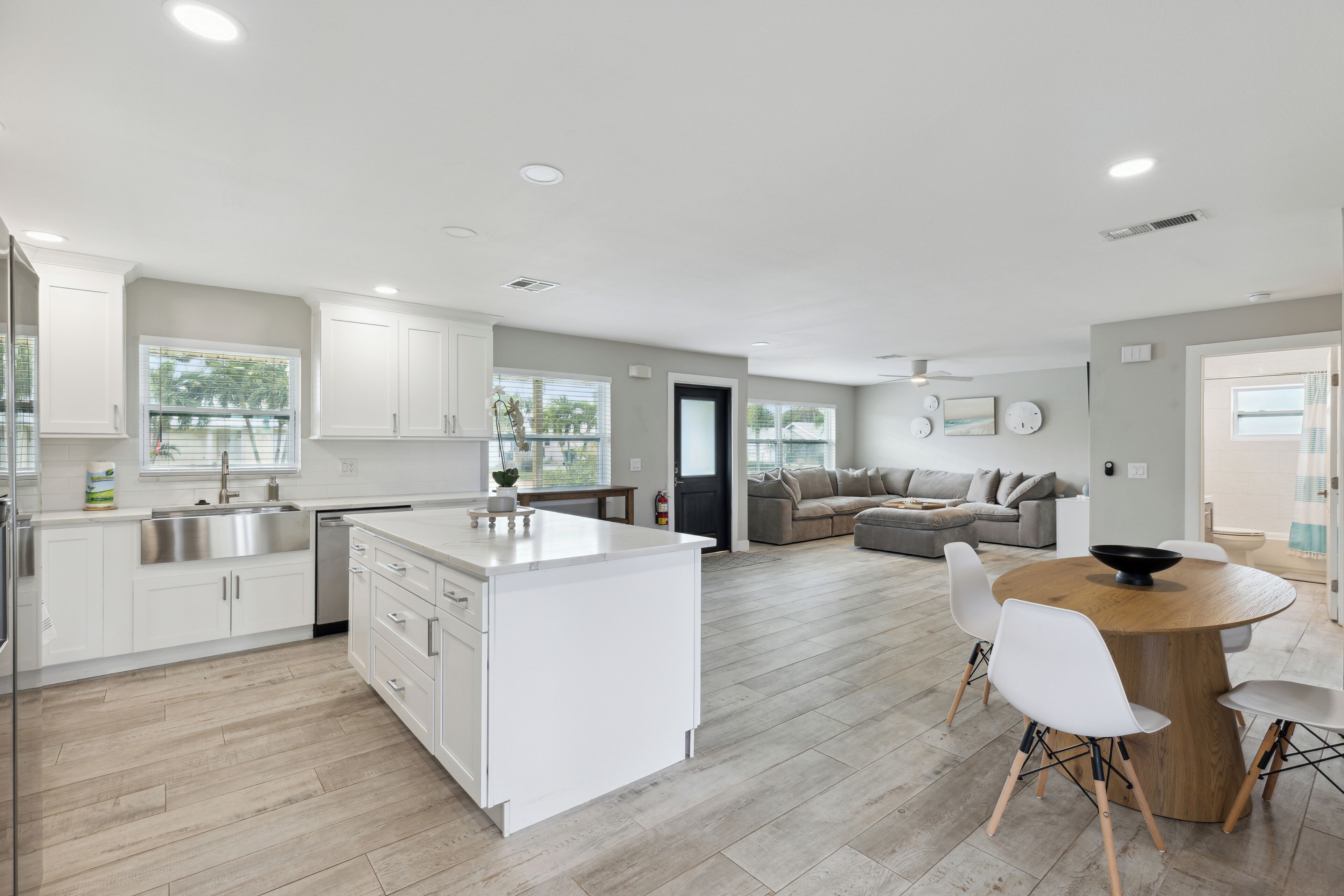 A modern kitchen with white cabinets, a central island, and a dining area with a round wooden table and white chairs.