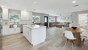 Una cocina moderna con armarios blancos, una isla central y un comedor con una mesa redonda de madera y sillas blancas.