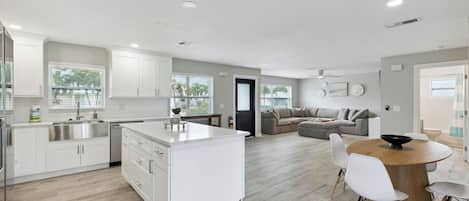 A modern kitchen with white cabinets, a central island, and a dining area with a round wooden table and white chairs.