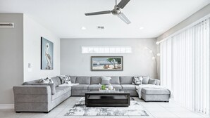 A modern living room with a grey sectional sofa, a black coffee table, and a ceiling fan. - Family Fun Beach Townhome w/ Pool, BBQ & Game Room! 🌊🏖️ (Indian Harbour Beach)