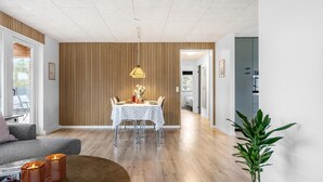 A modern living room with a dining area, wooden panel walls, and a large potted plant. - Amazing home in Vestervig with WiFi (Vestervig)