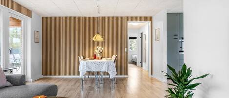 Un salon moderne avec un coin repas, des murs recouverts de panneaux en bois et une grande plante en pot.