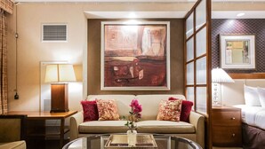 Une chambre d’hôtel avec un canapé, une table basse en verre, une lampe, un lit et un tableau au mur.