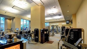 Une salle de sport équipée de divers appareils d’exercice, d’un téléviseur et de grandes fenêtres.