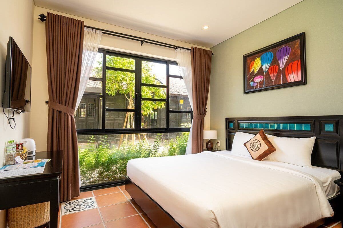 Una camera d'albergo con un letto grande, una scrivania con un computer, una finestra con tende e un quadro appeso al muro.