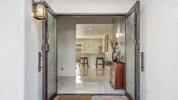 Un ingresso moderno con porta in vetro, una panca in legno e un vaso decorativo.
