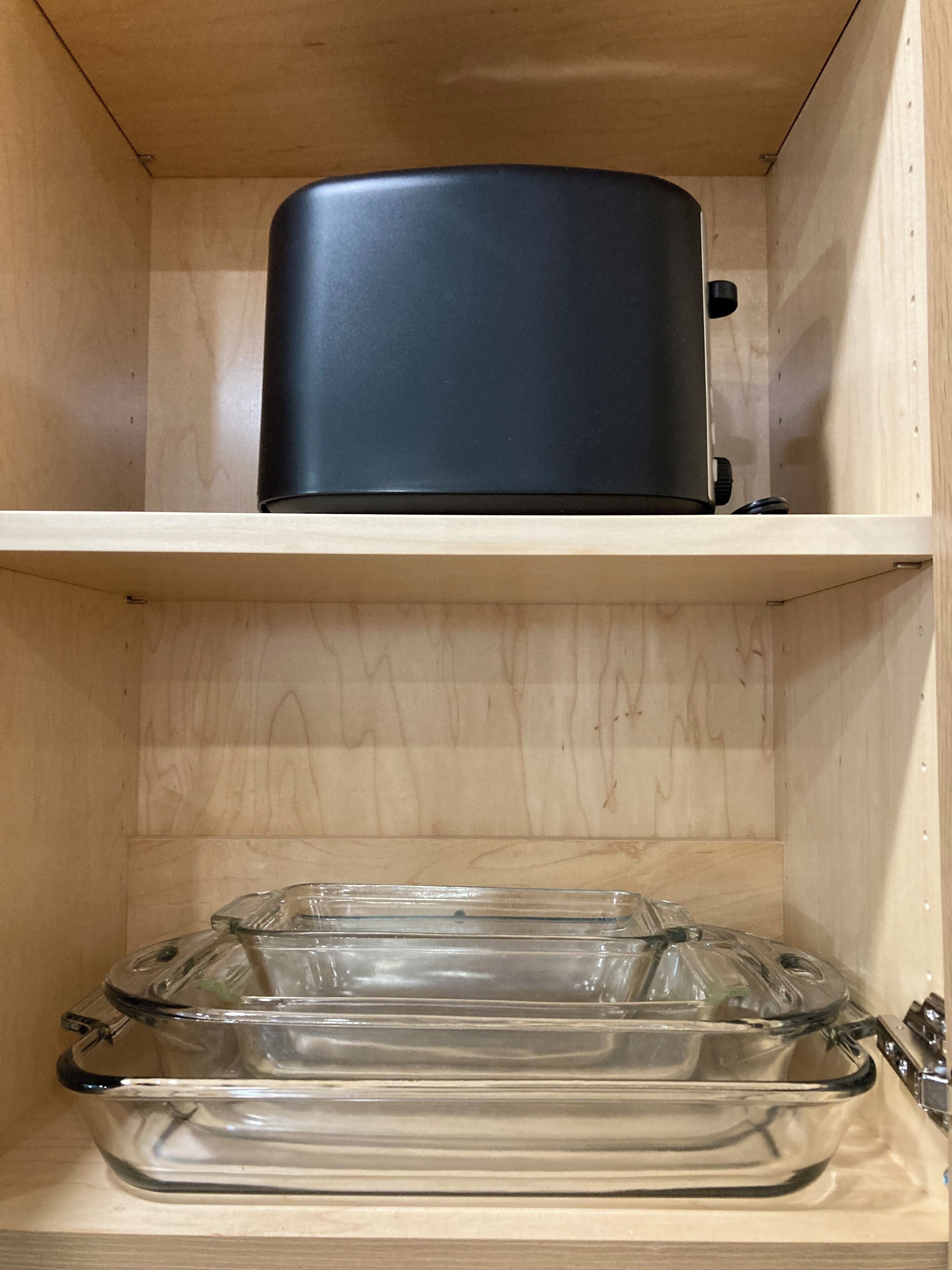 Un mueble de madera con un electrodoméstico negro en la repisa superior y un recipiente de vidrio transparente en la inferior.