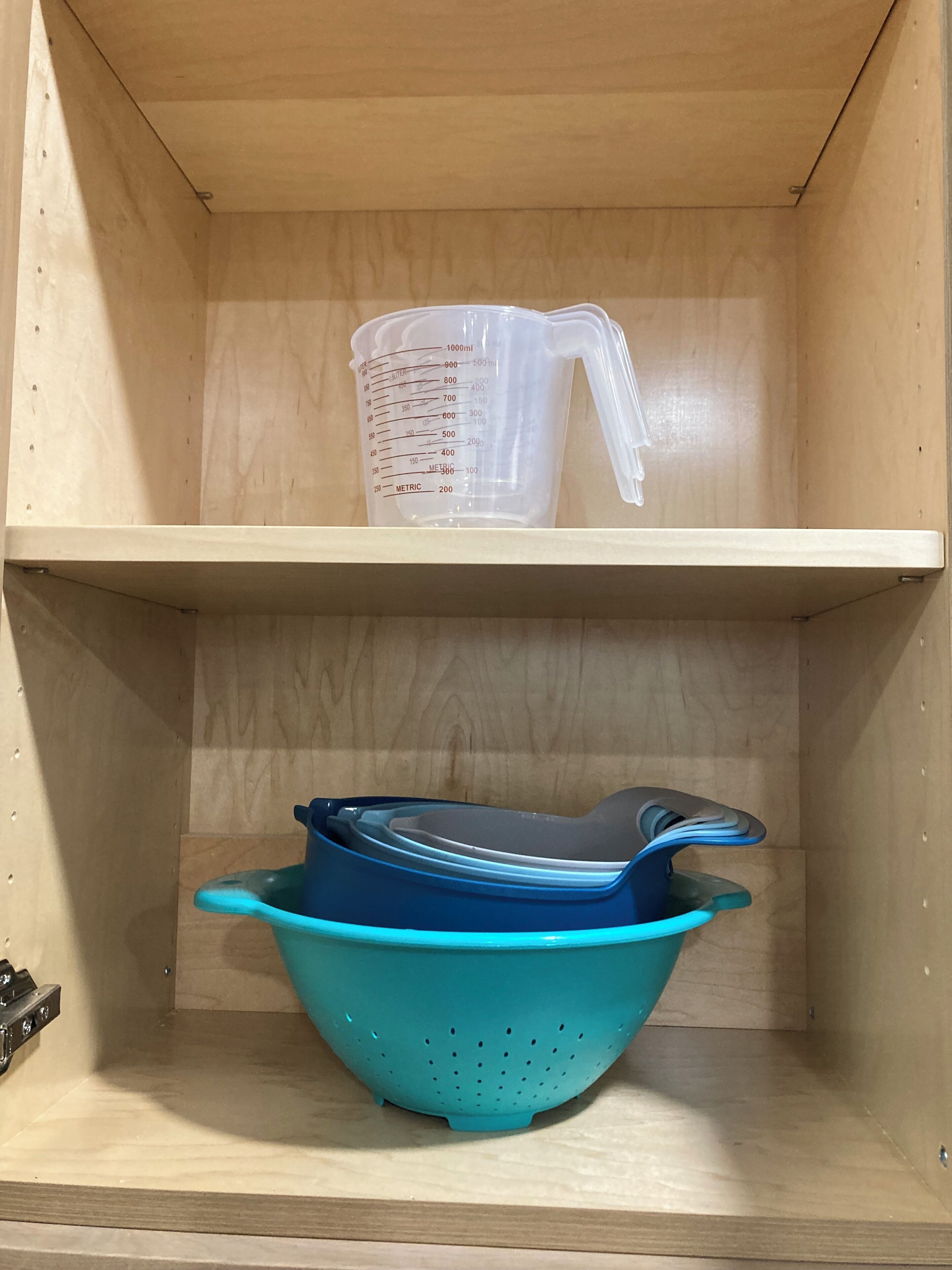 Una repisa de madera con un vaso medidor y un colador azul.