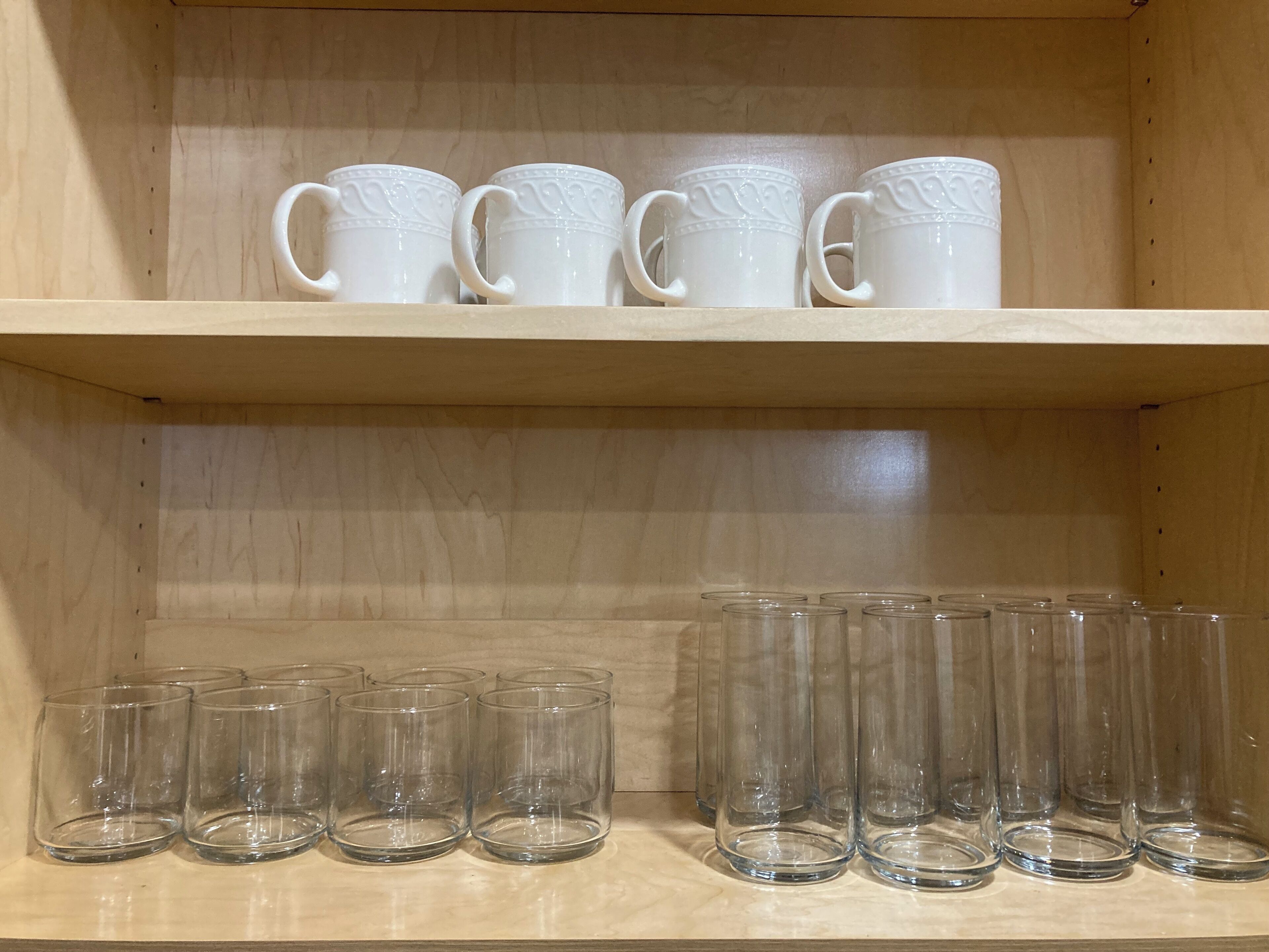 A shelf with white ceramic mugs and clear glass tumblers.