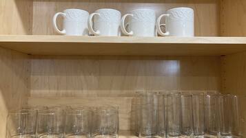 A shelf with white ceramic mugs and clear glass tumblers.