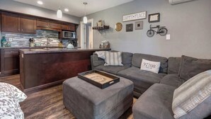 Une cuisine moderne avec des meubles de couleur sombre, un îlot central et un canapé gris dans l’espace salon.