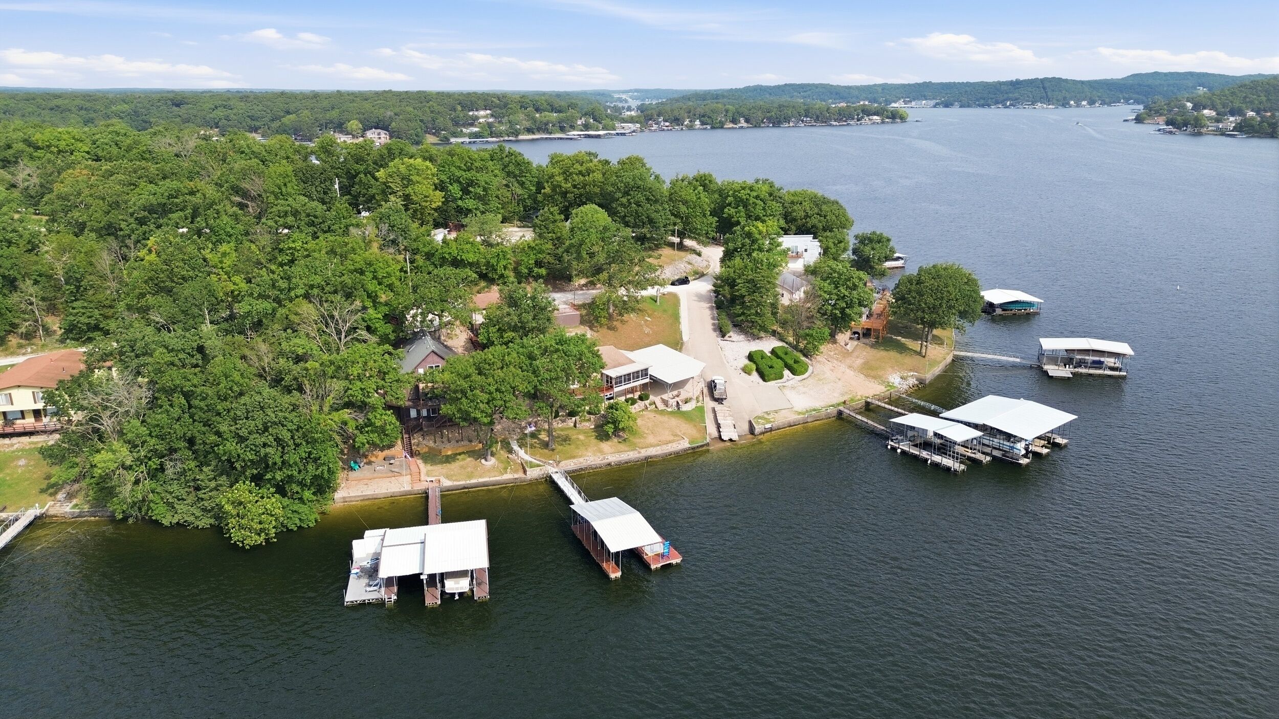 Vue aérienne d’une propriété au bord du lac, avec des bateaux amarrés, un petit quai et un sentier menant à une maison.