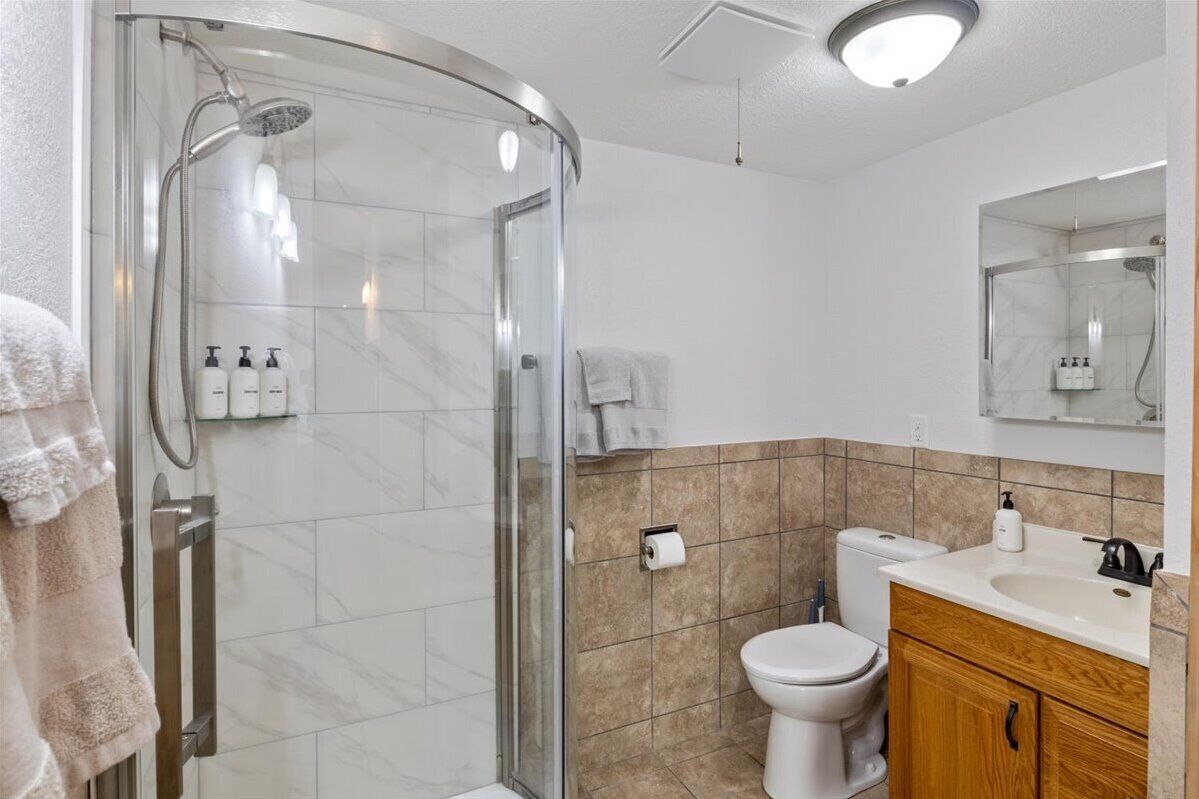 A modern bathroom with a glass-enclosed shower, a toilet, a sink with a mirror, and toiletries on the wall.