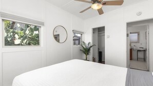 Quarto com cama, ventilador de teto, janela com planta e espelho.