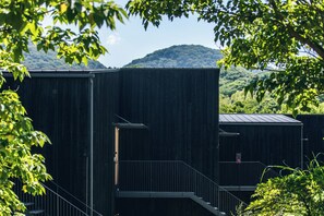 A modern building with a staircase leading to an upper level, surrounded by lush greenery and a mountainous backdrop. - JIJIJIN Mastsuyama (Tobe)