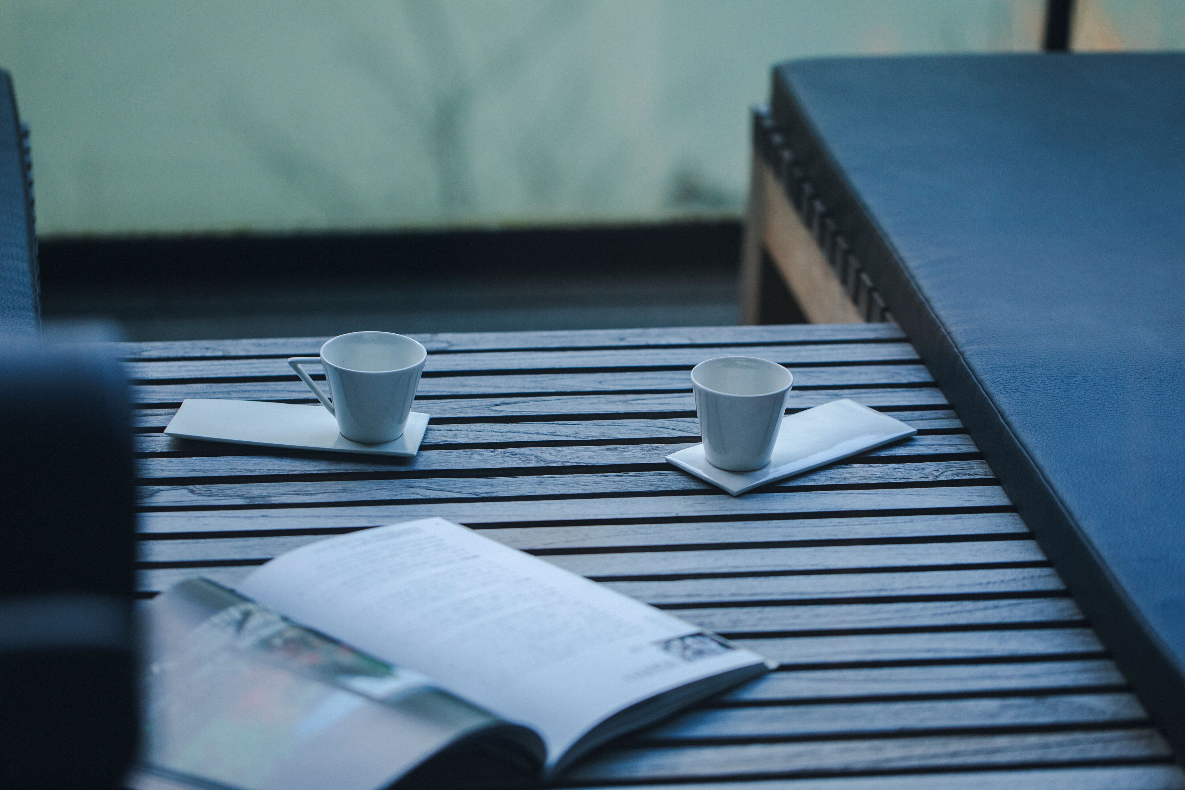 Una mesa de madera con dos tazas blancas y un libro.