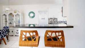 Une cuisine moderne avec un plan de travail noir, des armoires blanches et deux chaises en bois dont les dossiers sont ajourés.