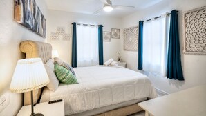 Une chambre à coucher comprenant un lit, une table de chevet avec une lampe, un ventilateur de plafond et des œuvres d’art décoratives accrochées au mur.