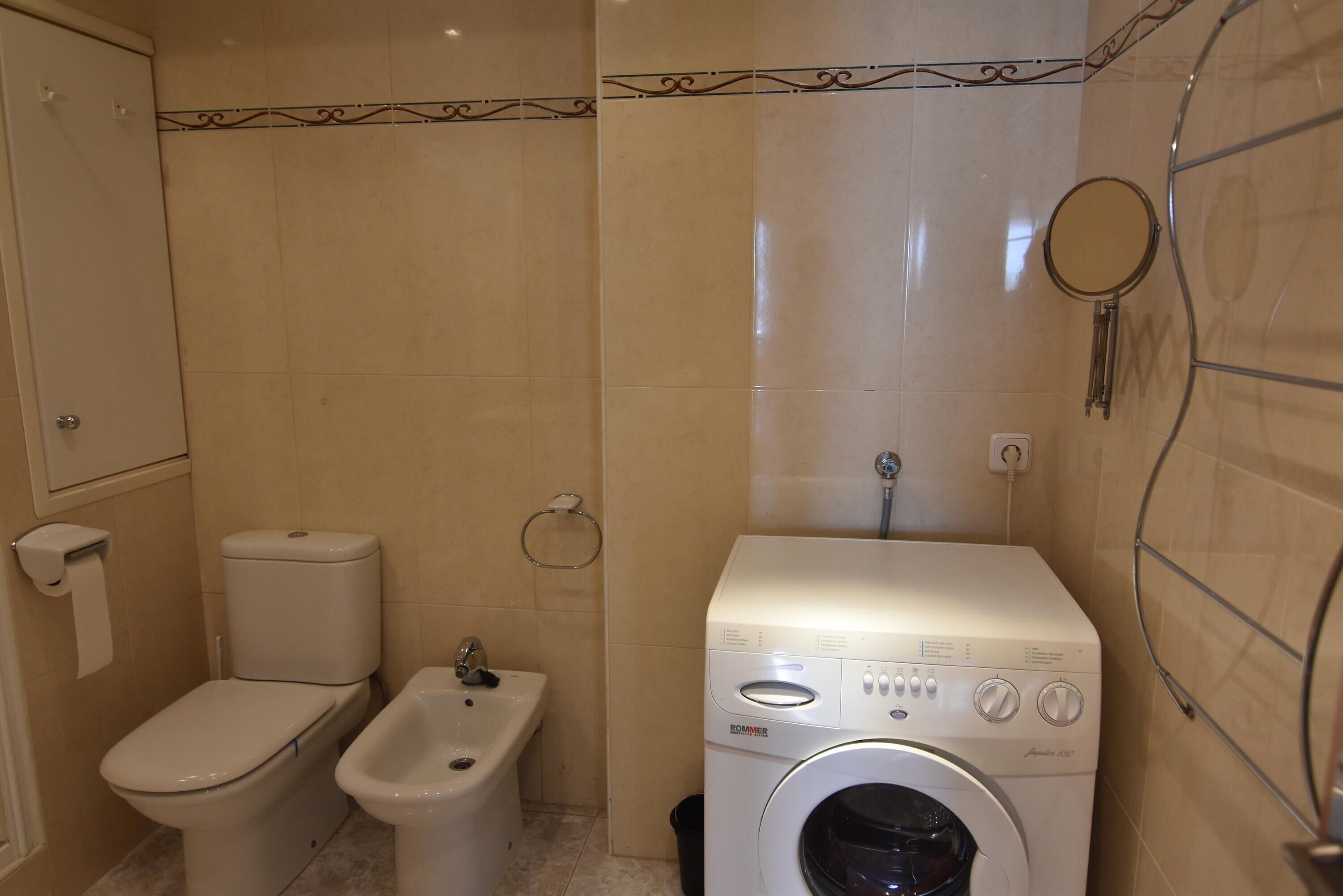 A compact bathroom with a toilet, bidet, and a front-loading washing machine.