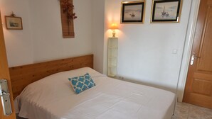A neatly made bed with a blue pillow, a wooden headboard, a wall-mounted lamp, and framed pictures on the wall. - Apartment in Roses with pool, close to the beach and center, ideal for a comfortable and relaxing holiday. (Roses)