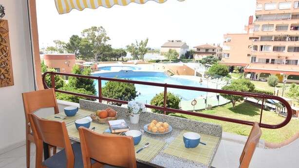 A balcony with a table set for breakfast, overlooking a swimming pool and residential buildings.