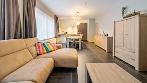 Ein modernes Wohnzimmer mit einer Couch, einem Couchtisch und einem Essbereich, im Hintergrund eine Küche.