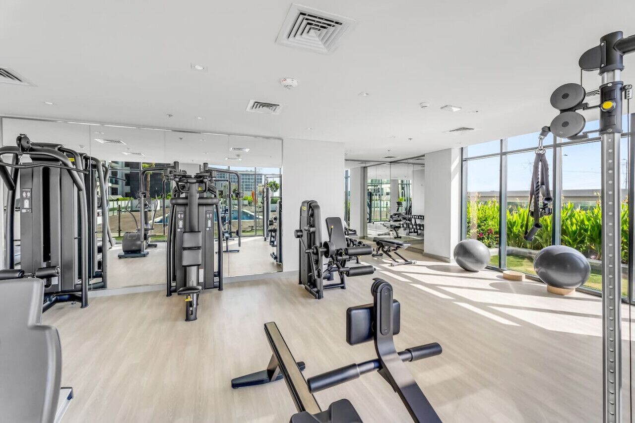 Une salle de sport moderne dotée de divers équipements d’entraînement, de grandes fenêtres et d’un aménagement propre et spacieux.