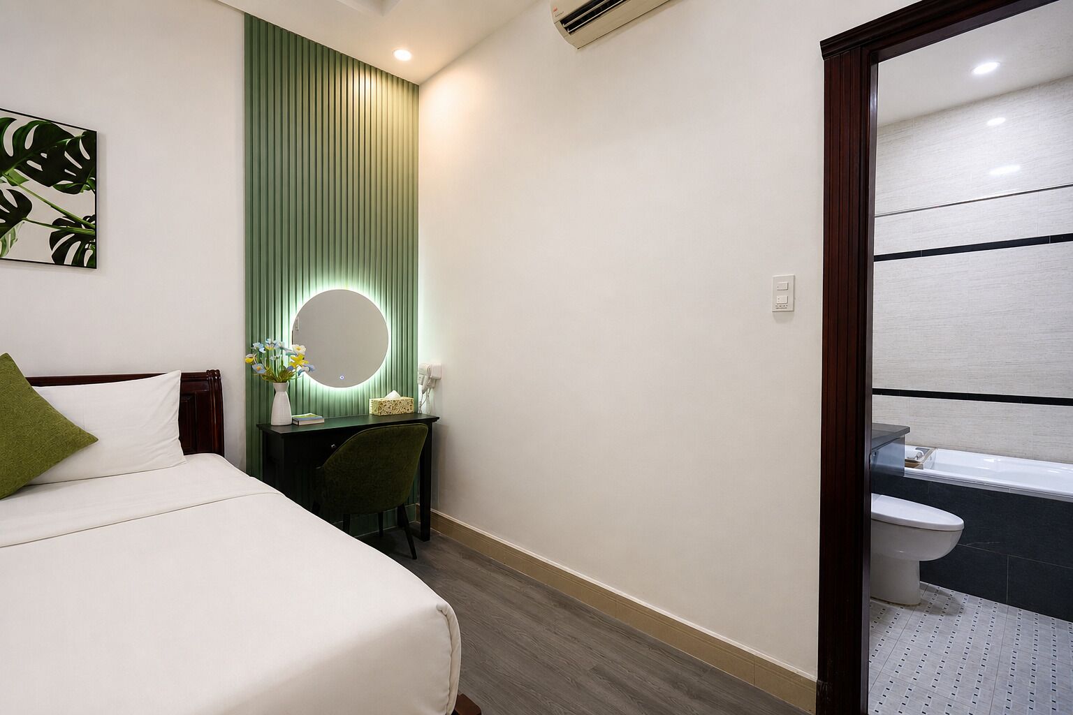 Ein Hotelzimmer mit Bett, Schreibtisch mit Spiegel, einer kleinen Pflanze und einem Badezimmer mit Toilette und Badewanne.